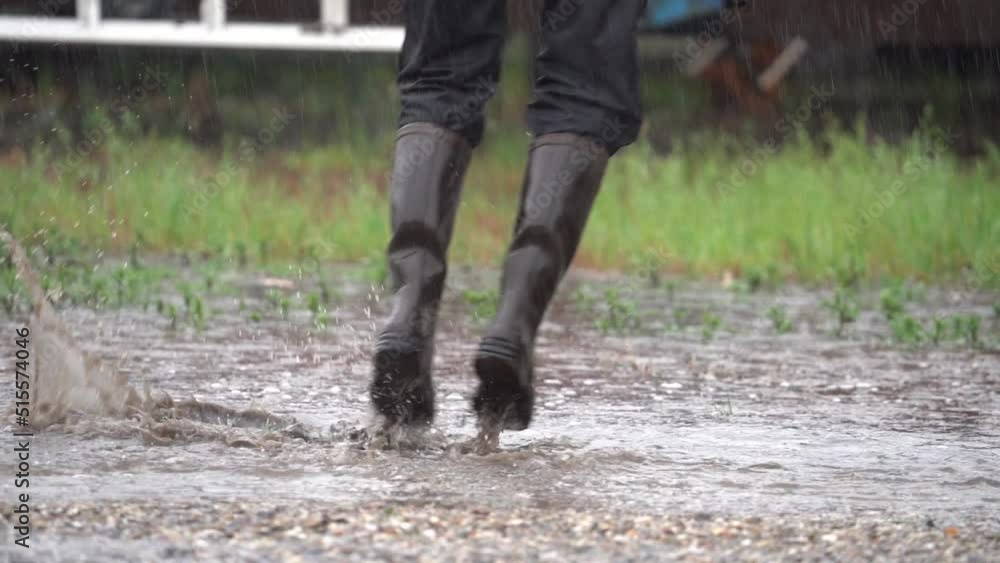 Feet Of A Happy Person Wearing Black Boots Is Jumping Over Rain Puddles On Rainy Day. Close Up Feet Of A Happy Person Wearing Black Boots Is Jumping Over Rain Puddles On Rainy Day. Close Up