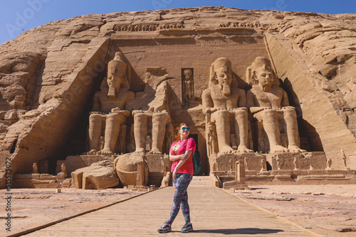 White Woman Tourist in front of the Colossal Statues of Ramesses II seated on a throne near the entrance to the Great Temple at Abu Simbel, Egypt