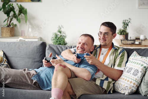 Gay couple relaxing on sofa in embrace and playing video game on console during leisure time