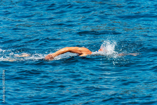Male freestyle swimmer (front crawl) in the blue waves of the Mediterranean sea, side view.