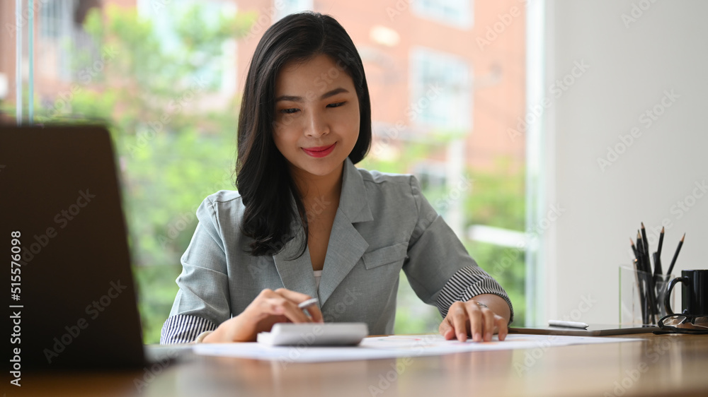 Professional young businesswoman using calculator and preparing annual financial report at office desk Professional young businesswoman using calculator and preparing annual financial report at office desk