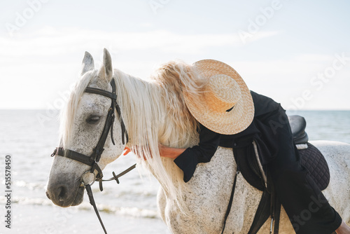 Young blonde woman in black clothes riding white horse on seascape background