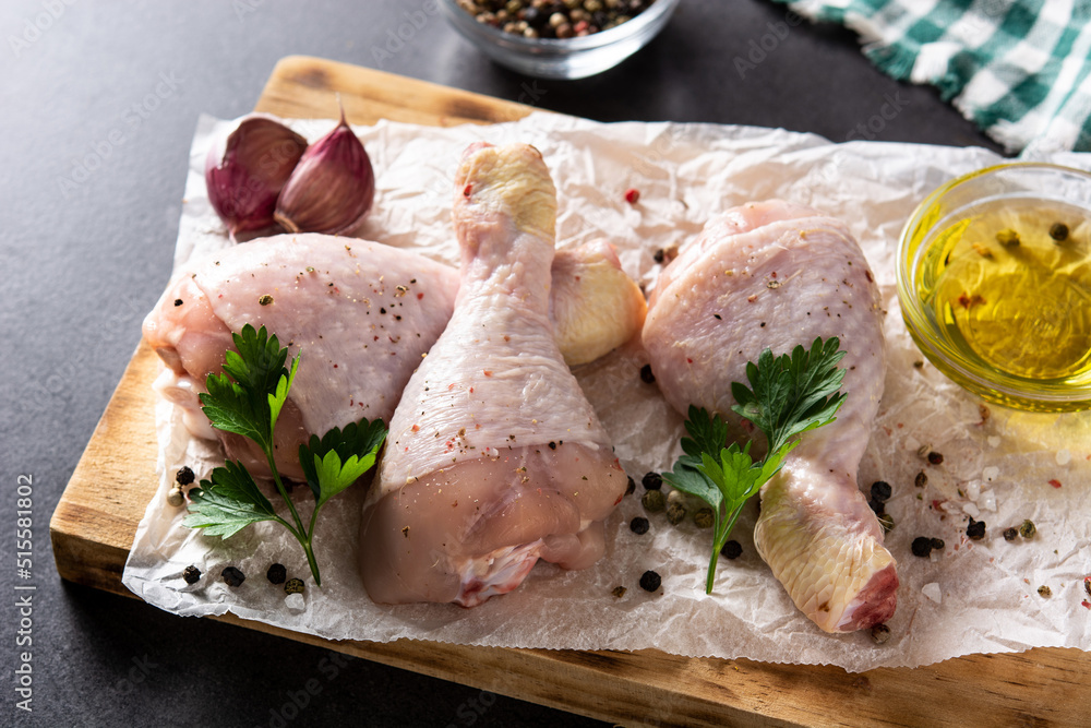 Raw chicken meat legs with spices and herbs on black background Raw chicken meat legs with spices and herbs on black background