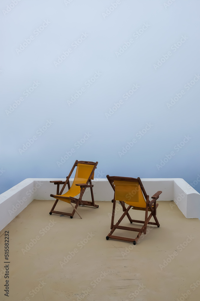 View of two empty sunbeds in front of the aegean sea that is covered by fog in Santorini Greece