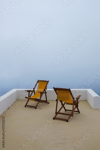 View of two empty sunbeds in front of the aegean sea that is covered by fog in Santorini Greece