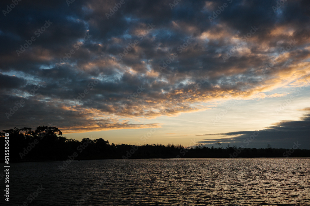 Dramatic sunrise sky covered by clouds make darkness to the water and land.