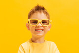 Portrait of smiling little boy, child in bright T-shirt and sunglasses posing isolated over yellow background