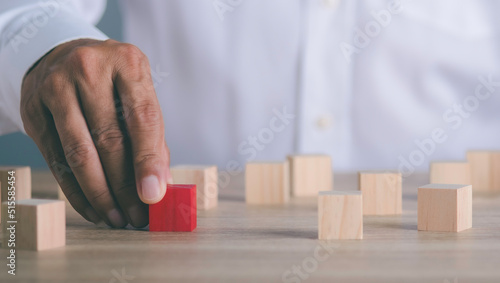 The young businessman goes to the red wooden block that is placed on the table ,