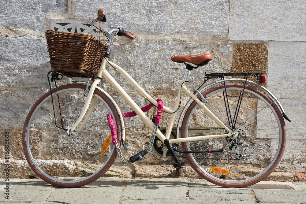 Women's bicycle with basket closed with chain against a wall in a italian street paved of stone