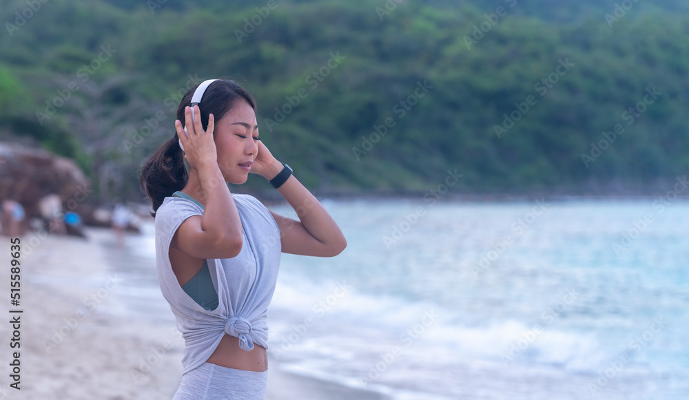 Portrait Asian joyful tanned woman relaxing with favorite music at beach show smiling happiness with headphones spending holiday summer on beach. Portrait Asian joyful tanned woman relaxing with favorite music at beach show smiling happiness with headphones spending holiday summer on beach.