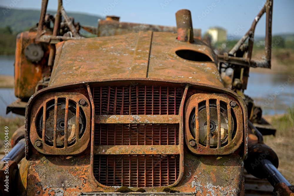 Broken headlights and the radiator of an old rusty crawler vehicle seen from the front at a gravel pit Broken headlights and the radiator of an old rusty crawler vehicle seen from the front at a gravel pit