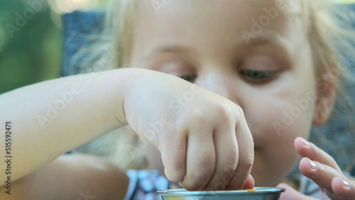 Little girl eat french fries. Close-up of blonde girl takes potato chips with her hands and tries them sitting in street cafe on the park.