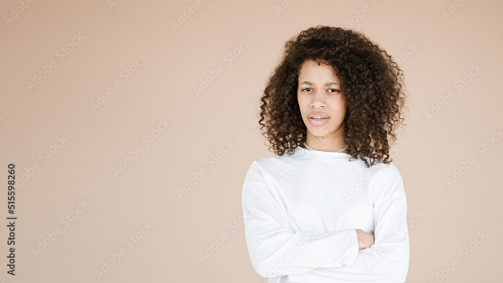 Displeased curly woman looks angrily at camera, smirks and looks from eyebrows, offended by boyfriend, focused at camera, standing upbeat against brown background Displeased curly woman looks angrily at camera, smirks and looks from eyebrows, offended by boyfriend, focused at camera, standing upbeat against brown background