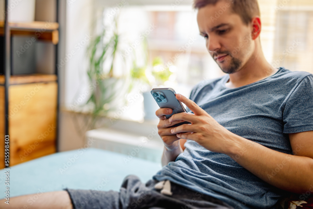 Fototapeta premium The guy sends messages from a modern smartphone in a bright modern home interior - the concept of chatting via social media
