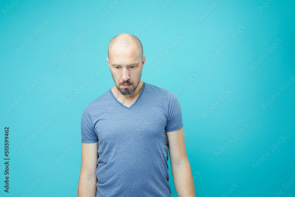 Close up of unhappy bald man in blue shirt on blue wall background. Close up of unhappy bald man in blue shirt on blue wall background.