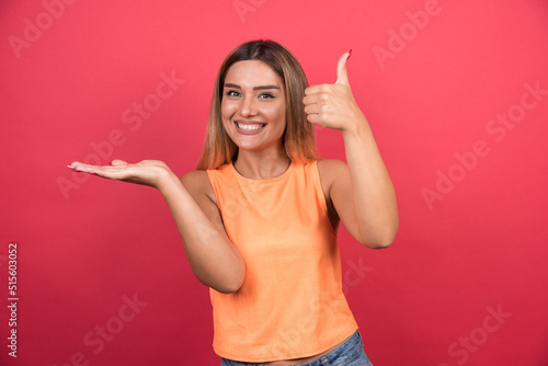 Pretty young woman making thumbs up on red background