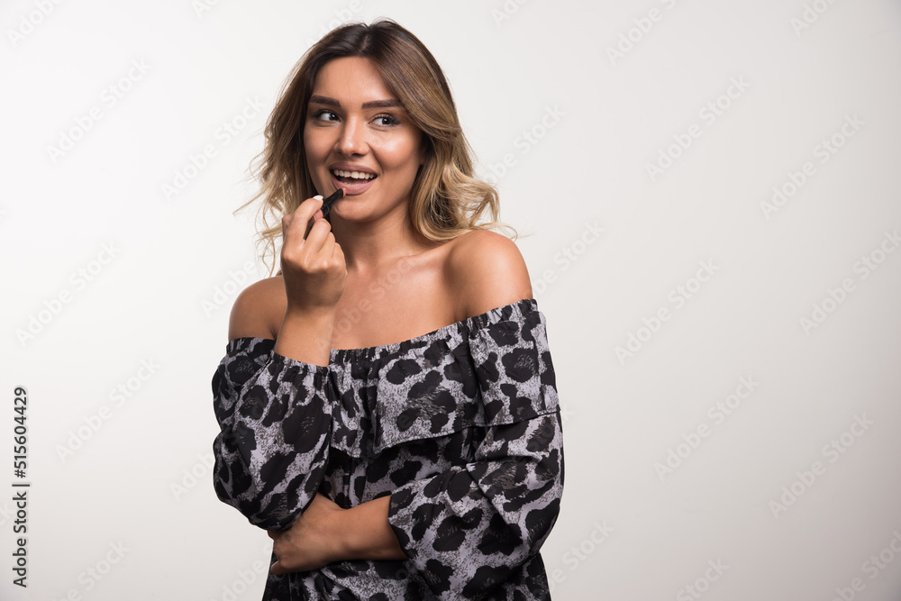 Young woman applying lipstick on white background while looking at side Young woman applying lipstick on white background while looking at side