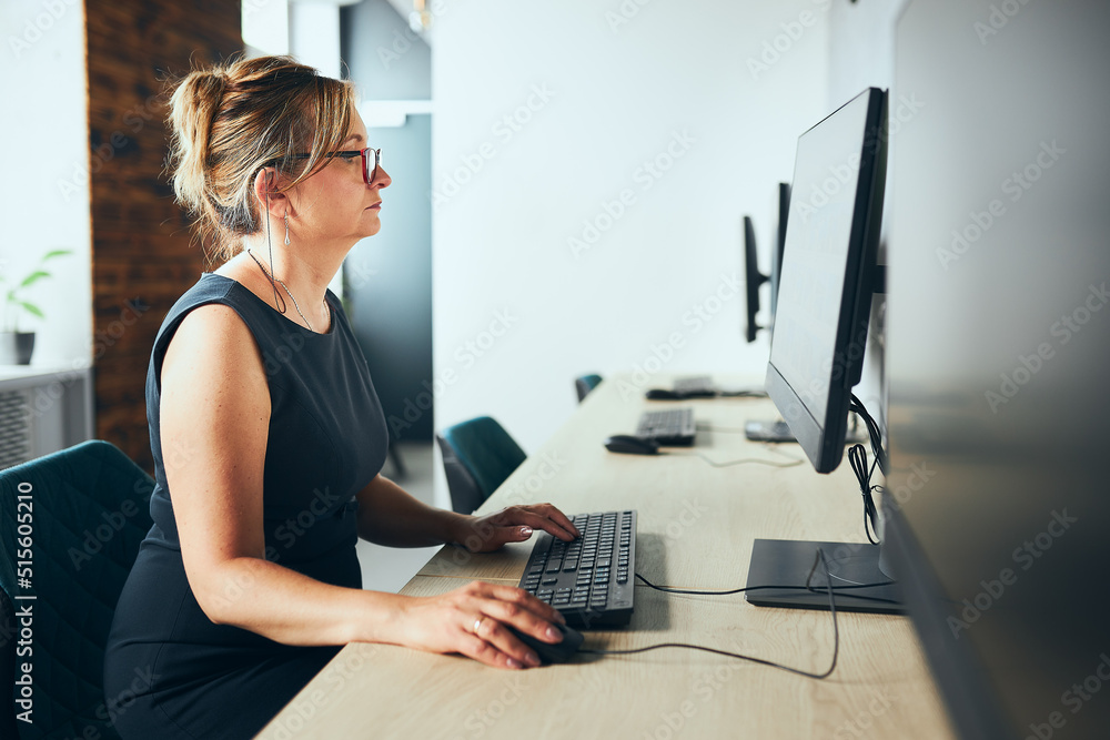 Concerned businesswoman working on computer in office. Busy woman sitting at desk at front of computer monitor. Focusing on work. Open office. Copy space right Concerned businesswoman working on computer in office. Busy woman sitting at desk at front of computer monitor. Focusing on work. Open office. Copy space right