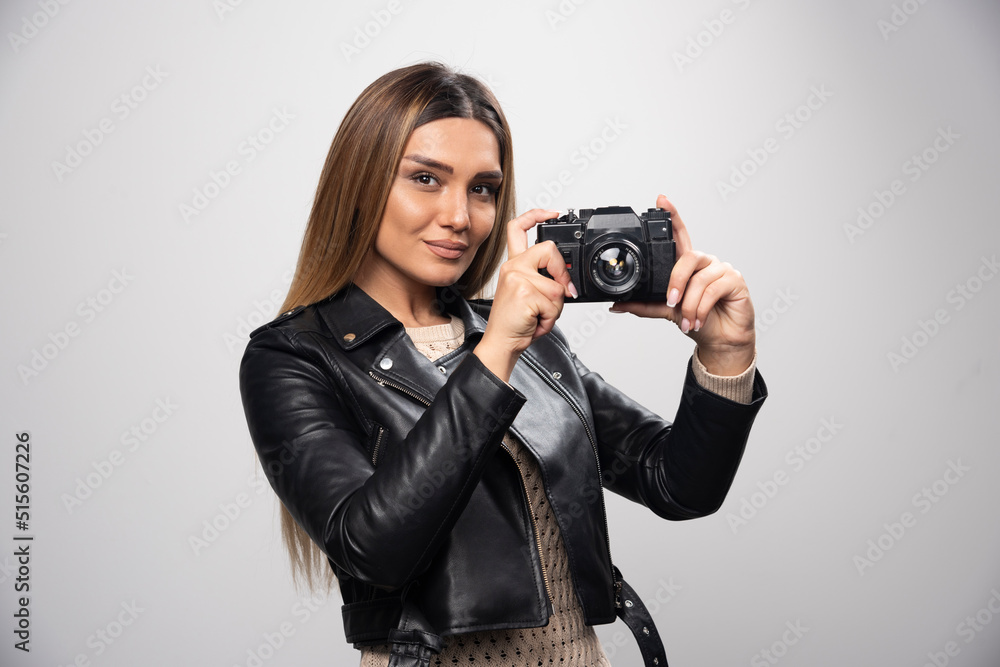 Blonde girl in black leather jacket taking her selfies with a camera Blonde girl in black leather jacket taking her selfies with a camera
