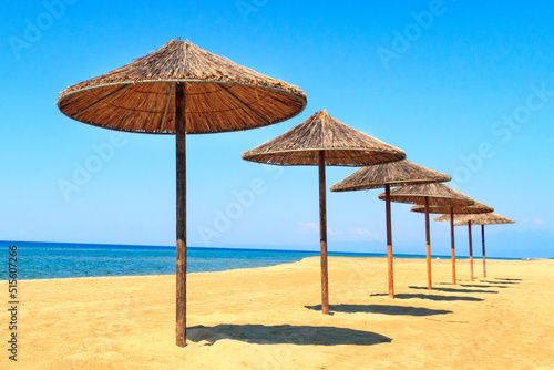 Row of wooden umbrellas at sandy beach, sea and blue sky vacation background, Greece
