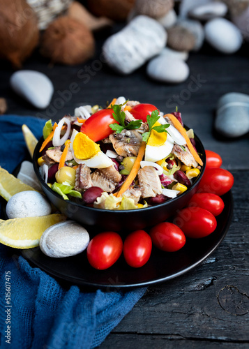 Fish salad with sardines, harringe, tuna, tomato, lemon, lettuce, cabbage, olives, beans, corn, carrotes and eggs on rustic kitchen table photo