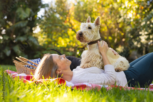 Happy mid adult caucasian lesbian woman with scottish terrier on stomach lying on blanket in yard