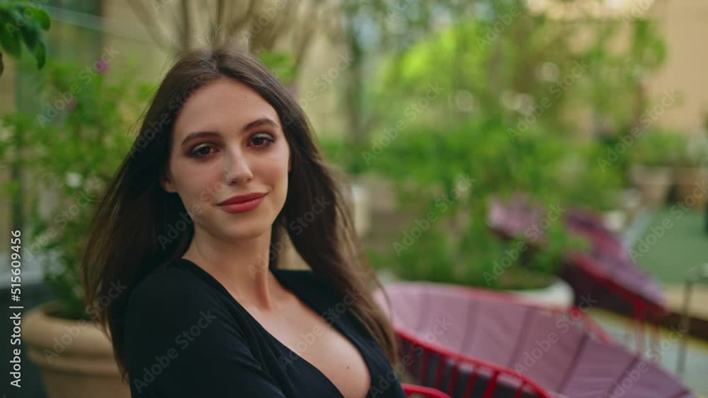 A beautiful young girl sm in a black dress with long dark hair in slippers sits on a chair in a restaurant on the street. The girl looks into the camera. Slow motion. Portrait of a girl A beautiful young girl sm in a black dress with long dark hair in slippers sits on a chair in a restaurant on the street. The girl looks into the camera. Slow motion. Portrait of a girl