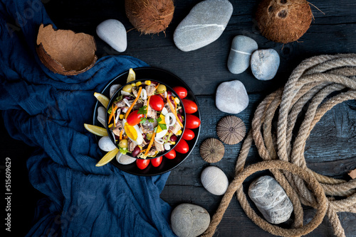 Fish salad with sardines, harringe, tuna, tomato, lemon, lettuce, cabbage, olives, beans, corn, carrotes and eggs on rustic kitchen table. Fresh and delicous seafood. Top view photo photo