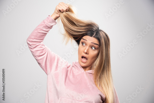 Blond lady in pink sweatshirt feels dissatisfied about her dry hair or hair color