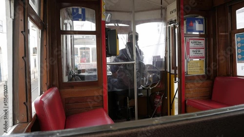Commute inside of historical Lisbon tram .Vintage wooden cabin interior and red seats. Driver cockpit at the front moving control handle. Big wheel on his side and fire extinguisher.