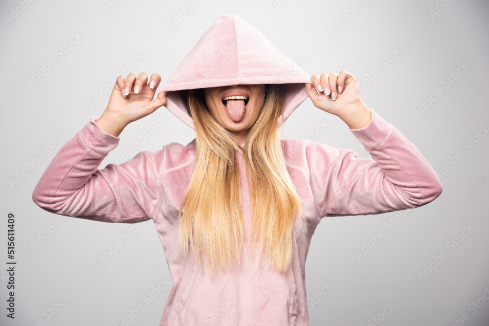 Blonde lady in pink sweatshirt making joyful and positive poses by wearing hoodie to her head