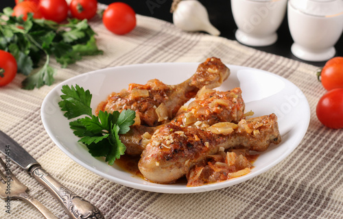 Baked chicken drumsticks with vegetables, spices and parsley on white plate