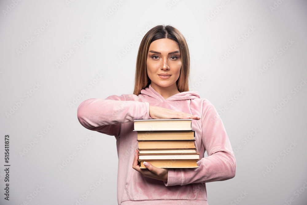 Girl in pink swaetshirt holding and carrying heavy pile of books Girl in pink swaetshirt holding and carrying heavy pile of books