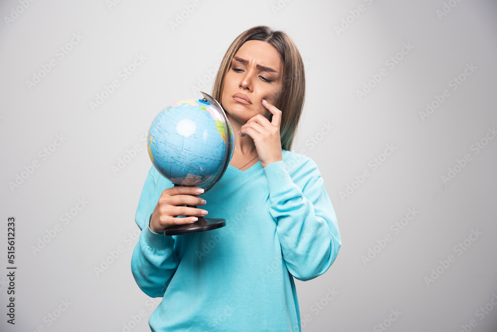 Blonde girl in blue sweatshirt holding a globe, thinking carefully and trying to remember Blonde girl in blue sweatshirt holding a globe, thinking carefully and trying to remember