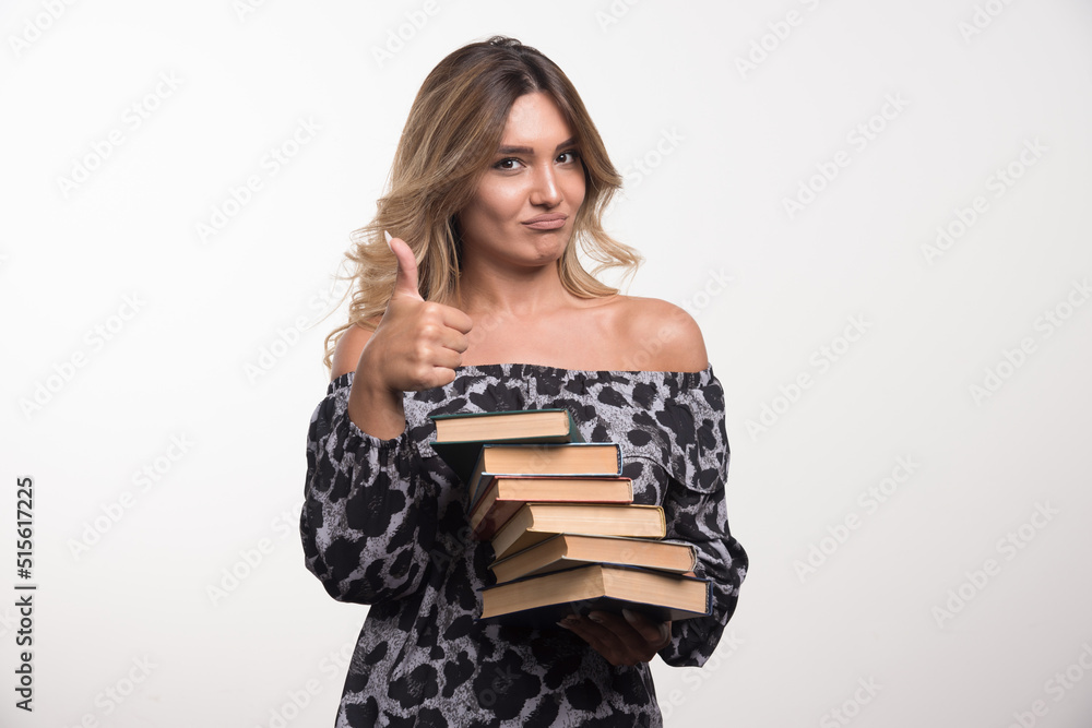 Young woman holding books showing thumbs up on white background