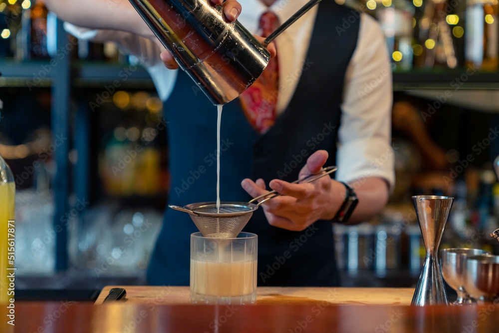 Professional male bartender preparing and serving cocktail drink to customer on bar counter at luxury nightclub. Barman making mixed alcoholic drink for celebrating holiday party at restaurant bar.