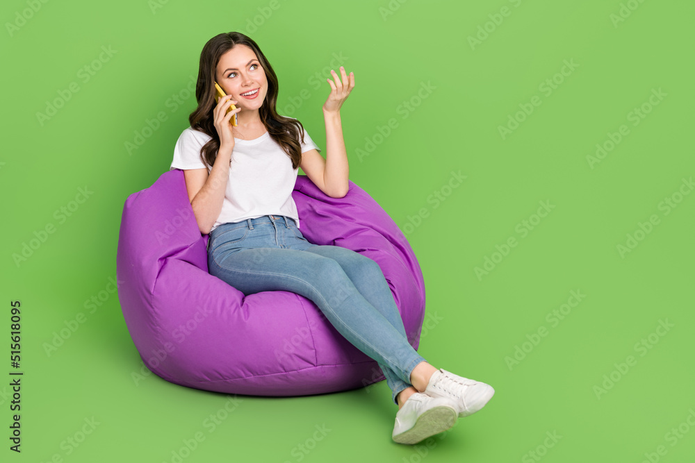 Photo of pretty dreamy woman dressed white t-shirt sitting bean bag talking gadget empty space isolated green color background Photo of pretty dreamy woman dressed white t-shirt sitting bean bag talking gadget empty space isolated green color background
