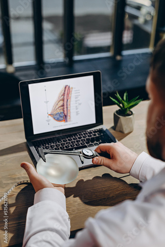 A plastic surgeon measures the size of a breast implant. On the background of a desktop with a laptop, and details.