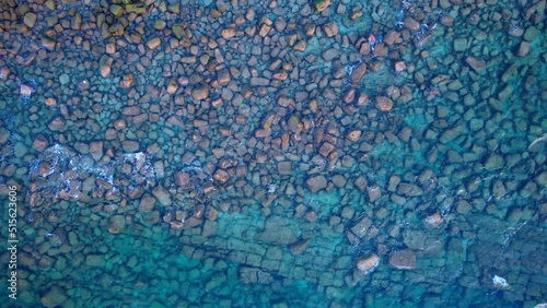 Drone top shot of tropical blue sea with waves over rocks.