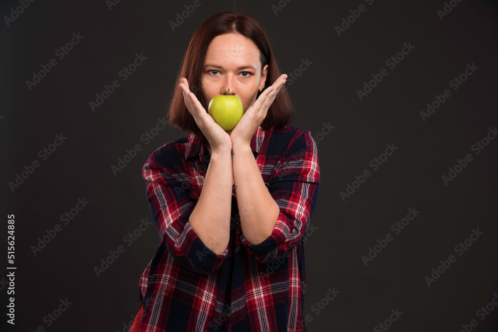 Female model in fall winter collection outfits holding a green apple on her mouth Female model in fall winter collection outfits holding a green apple on her mouth