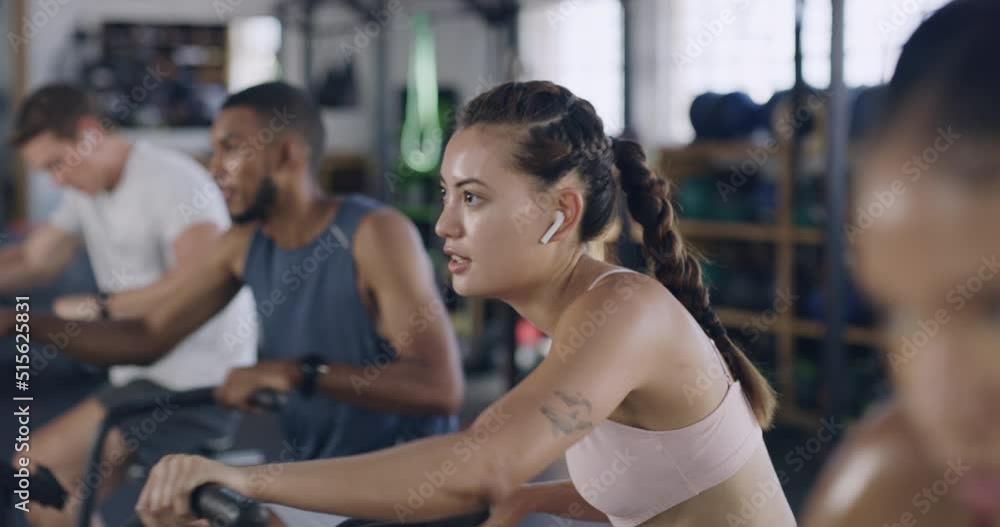 Focused and sporty woman during a spinning class at the gym. Fit people using air bikes for cardio exercise in a fitness facility. Group of sweaty men and women listening to music while exercising Focused and sporty woman during a spinning class at the gym. Fit people using air bikes for cardio exercise in a fitness facility. Group of sweaty men and women listening to music while exercising