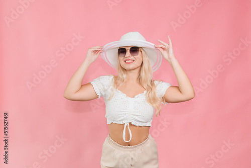 a young girl in a white hat and glasses poses on a pink background © Павло Товтин
