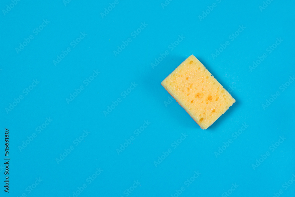 Yellow porous sponge for cleaning and washing dishes on a blue background with copy space. Homework concept.