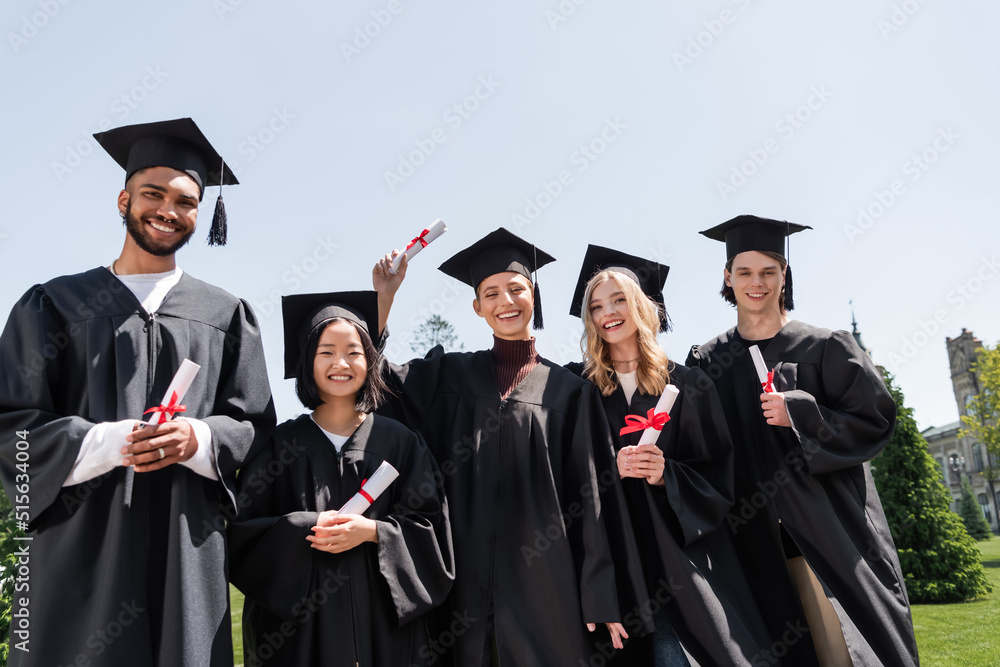 Multicultural bachelors holding diplomas outdoors. Multicultural bachelors holding diplomas outdoors.