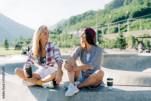 Portrait of two woman friends chatting while sitting in a skatepark. © Ilona