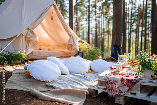 Beautiful white decor in boho style. Picnic in the nature, table, carpets, wigwam, tent, pillows in the park. Holidays in the nature concept.