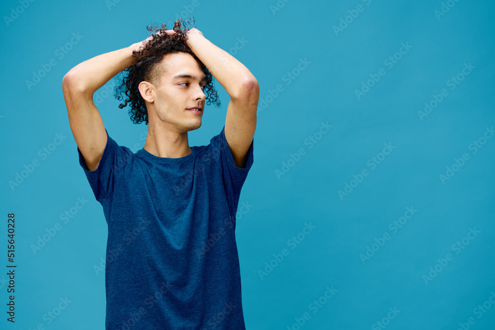 Positive joyful curly tanned Caucasian guy in basic t-shirt touches plays with hair curls posing isolated on over blue background. Lifestyle and Emotions concept. Good offer with copy space for ad Positive joyful curly tanned Caucasian guy in basic t-shirt touches plays with hair curls posing isolated on over blue background. Lifestyle and Emotions concept. Good offer with copy space for ad