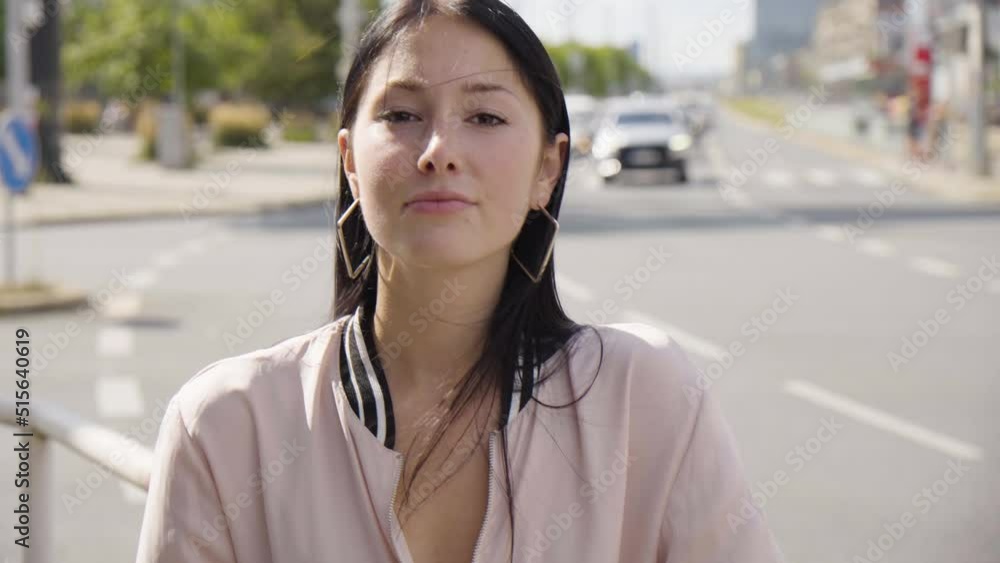 A young beautiful Caucasian woman shows a thumb up to the camera and nods with a smile in an urban area - closeup - a busy road in the background A young beautiful Caucasian woman shows a thumb up to the camera and nods with a smile in an urban area - closeup - a busy road in the background