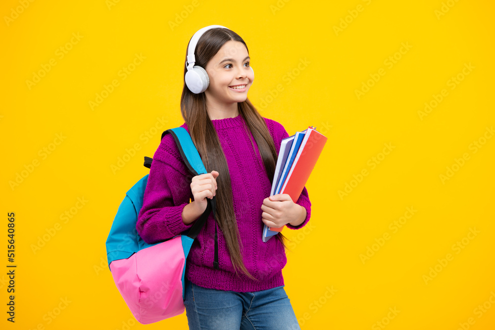 Schoolgirl, teenage student girl in headphones hold books on yellow isolated studio background. School and music education concept. Back to school. Schoolgirl, teenage student girl in headphones hold books on yellow isolated studio background. School and music education concept. Back to school.