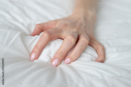 Woman hand tightly grips white sheet on bed